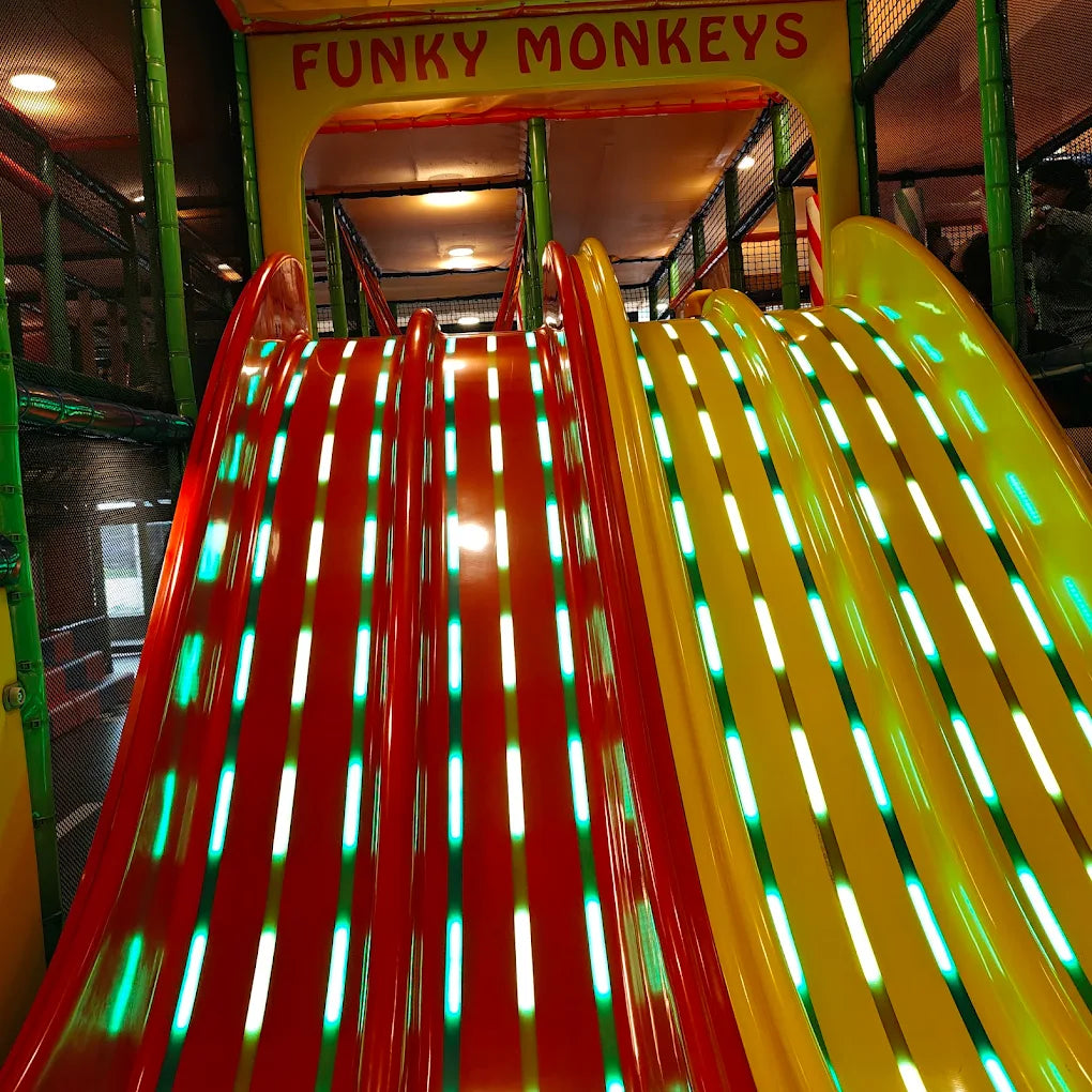 A brightly lit indoor playground with red and yellow slides, featuring the "Funky Monkeys" logo.