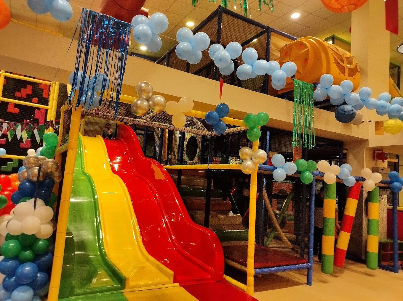 A colorful indoor playground with slides and balloons, featuring children playing.