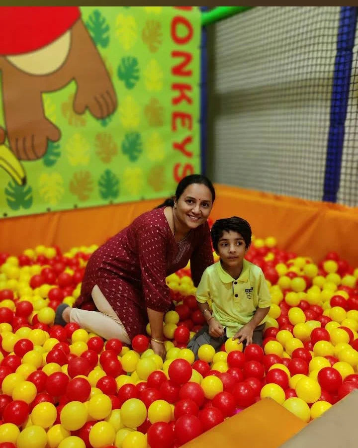A woman and a young boy sit in a ball pit filled with red and yellow balls.
