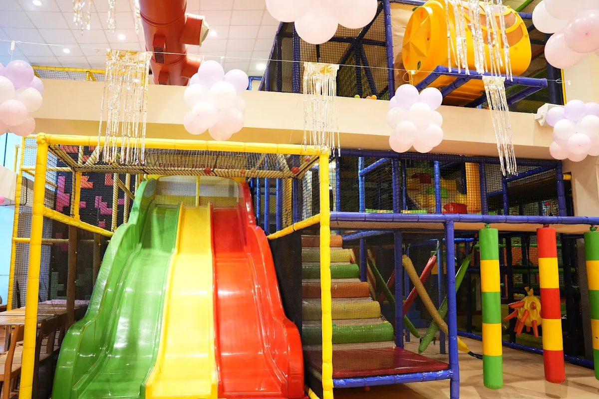 A colorful indoor playground with slides and climbing structures, decorated with balloons.
