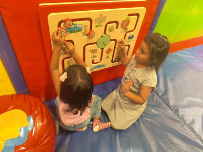 Two young children play with a colorful interactive maze board in a soft play area.