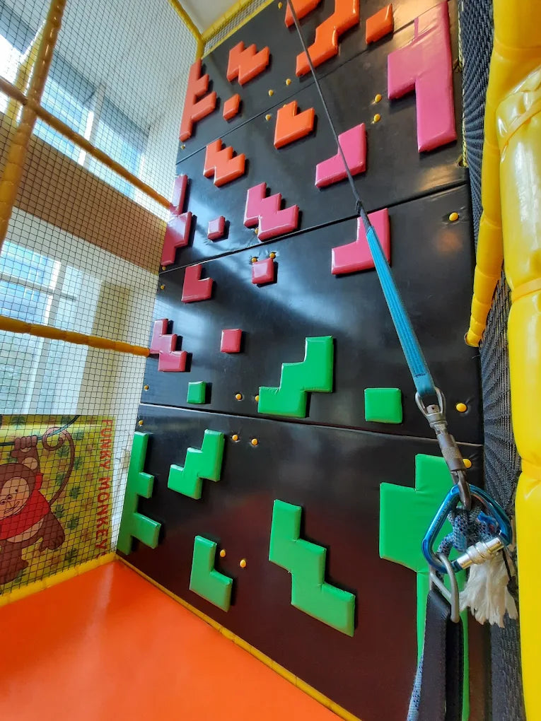A climbing wall with colorful holds and safety equipment in a children's play area.