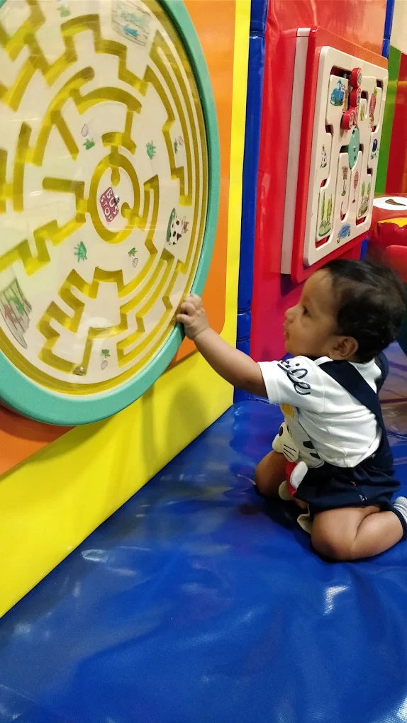 A baby plays with a maze toy in a colorful indoor playground.