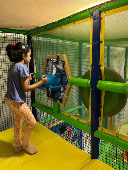 A young girl plays with a blue toy gun in a colorful indoor playground.