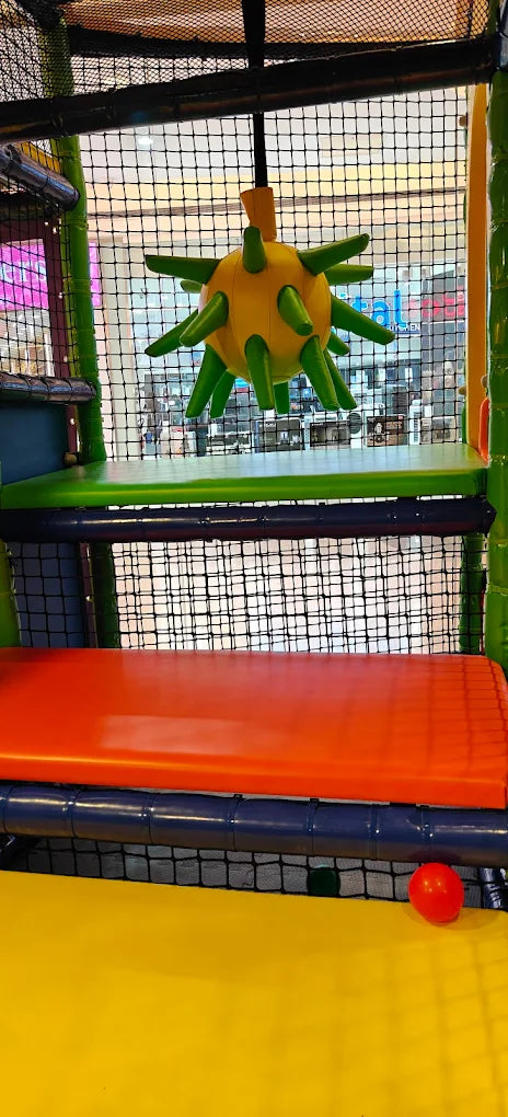 A colorful indoor playground with a spiky yellow and green toy hanging above an orange bench.