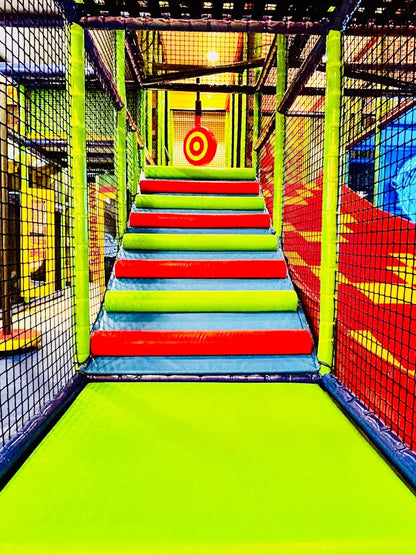 A colorful indoor playground with padded stairs and a target hanging above.