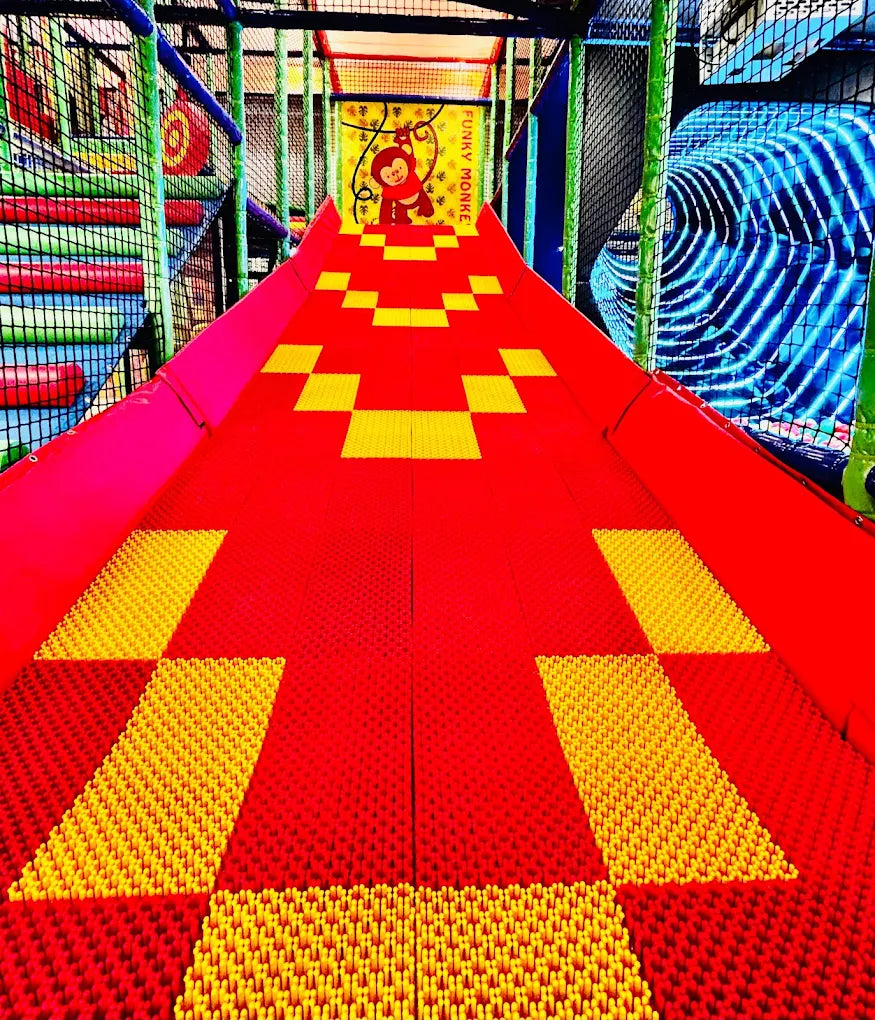 A colorful indoor playground slide with a monkey graphic at the top.