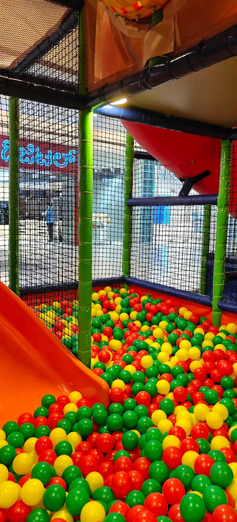 A ball pit filled with red, green, and yellow balls, with an orange slide and netting structure.