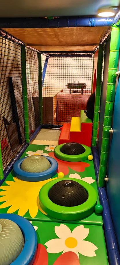Indoor soft play area with colorful mats, bouncy domes, and a slide for children.