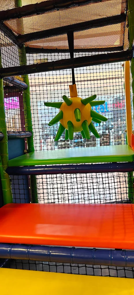 A yellow spiky ball hangs in a children's indoor play area with orange and green platforms.