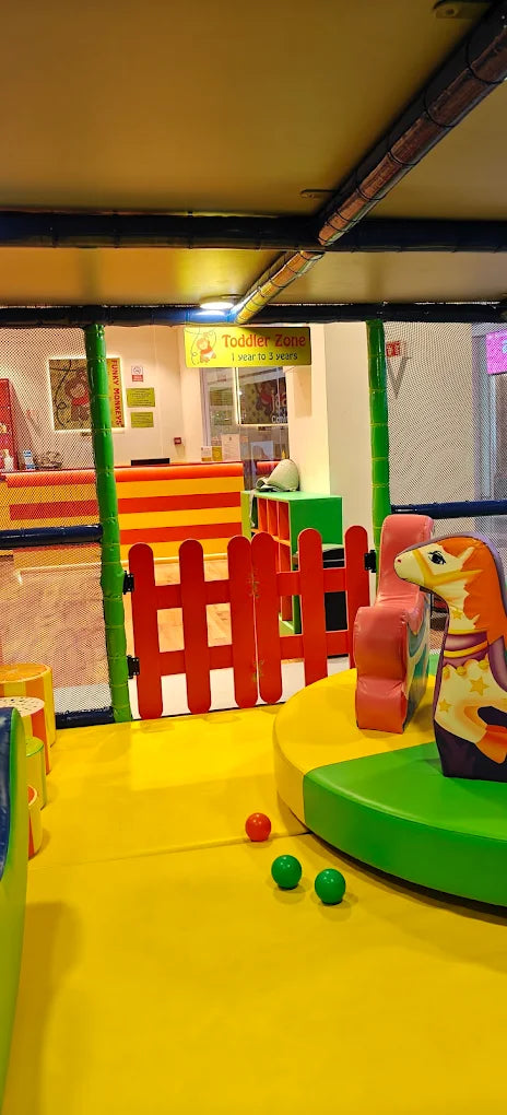 A colorful toddler play area with soft flooring, a rocking horse, and a "Toddler Zone" sign.