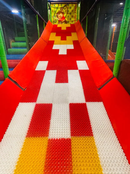 A colorful slide in a children's play area with a monkey graphic at the top.