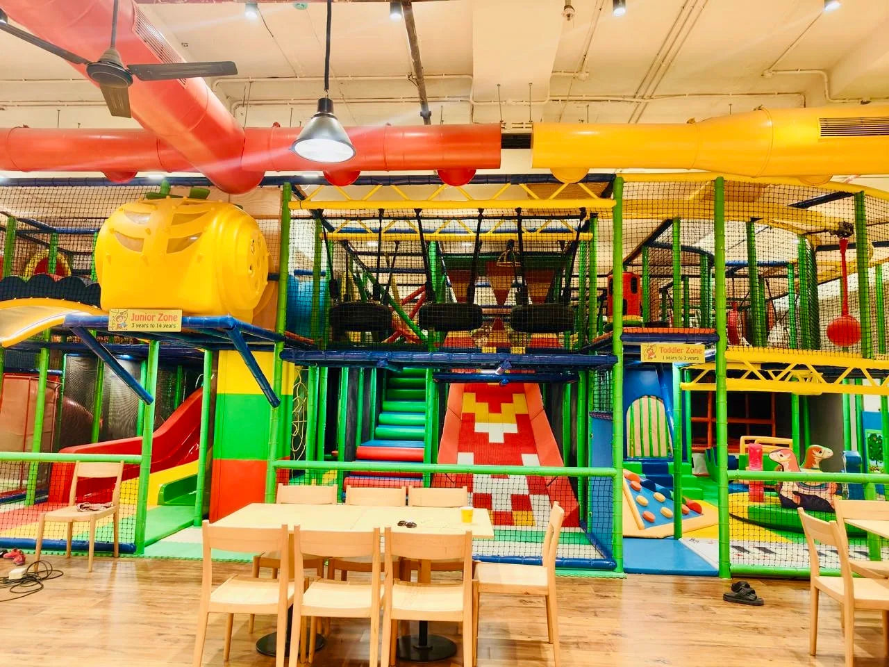 A colorful indoor playground with slides, climbing structures, and designated zones for different age groups.
