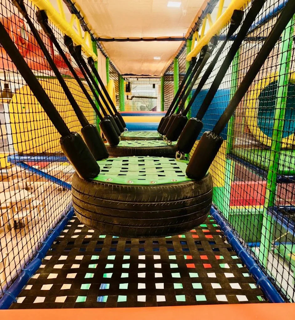 A rope bridge with tire platforms in a children's indoor playground.