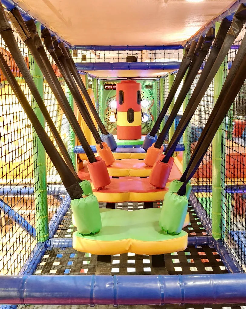 A colorful indoor playground with soft obstacles and swings for children.