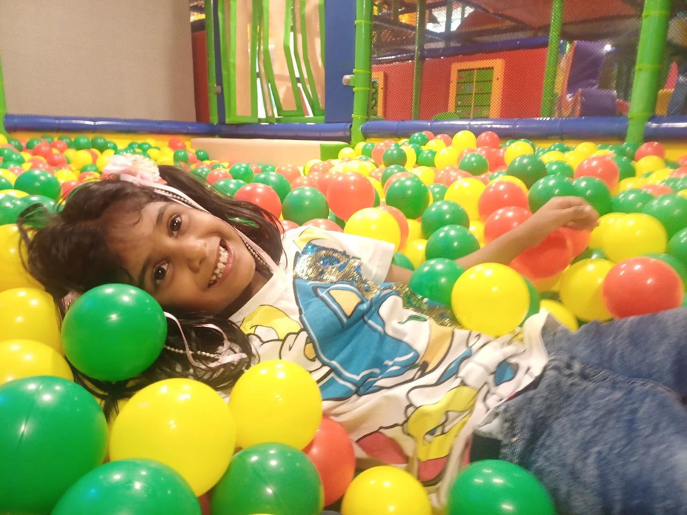 A young girl smiles while lying in a ball pit filled with colorful balls.