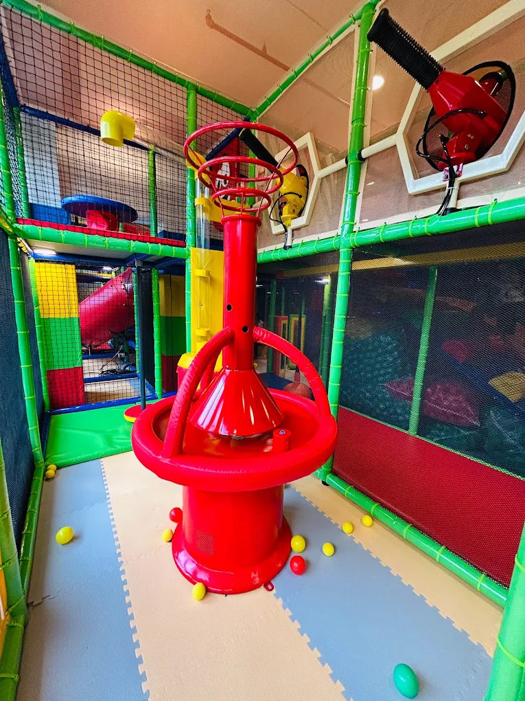 A colorful indoor playground with a red ball pit machine and soft flooring.