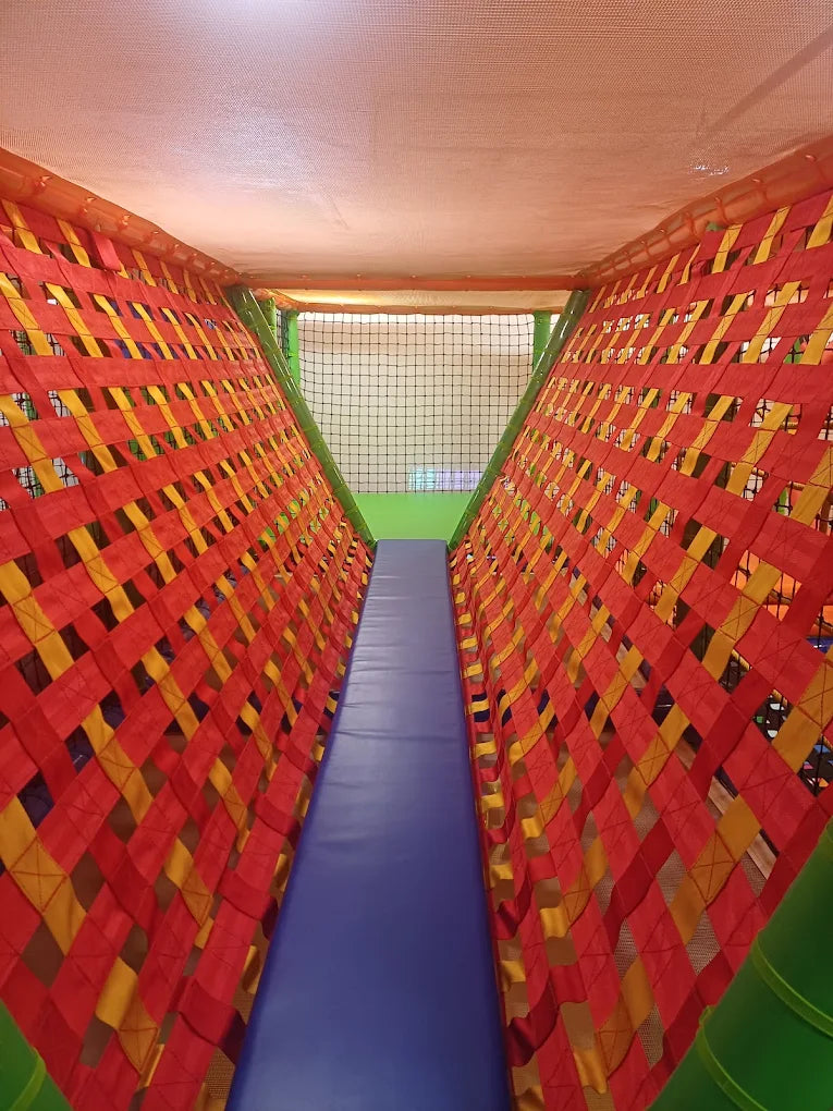 A colorful, netted tunnel in a children's play area with a blue slide.