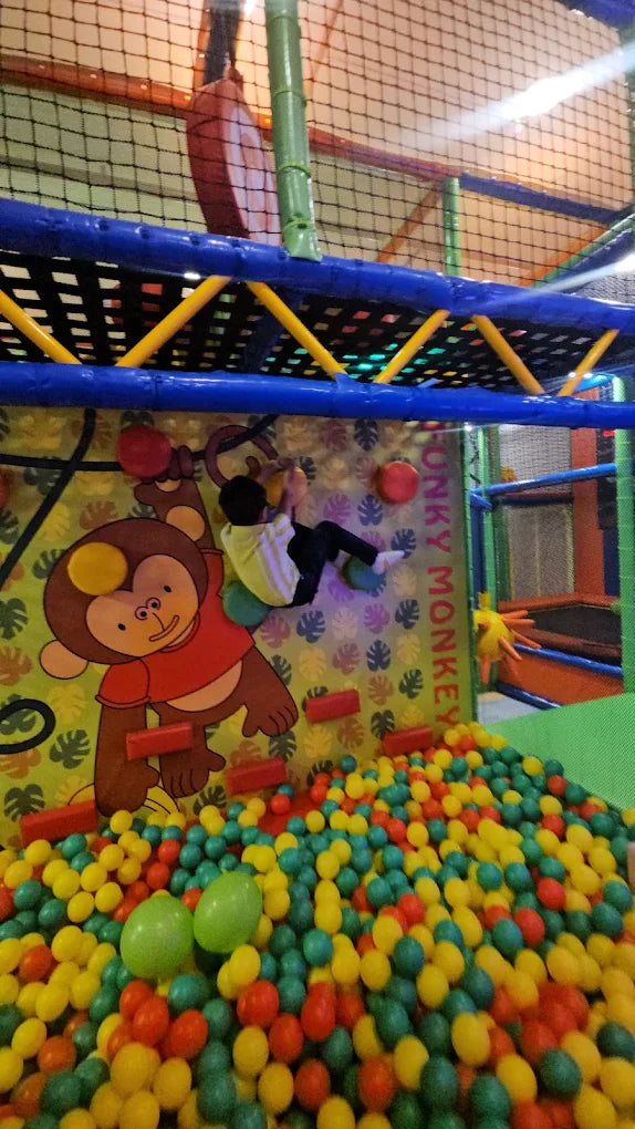 A child climbs a colorful wall in a ball pit play area.