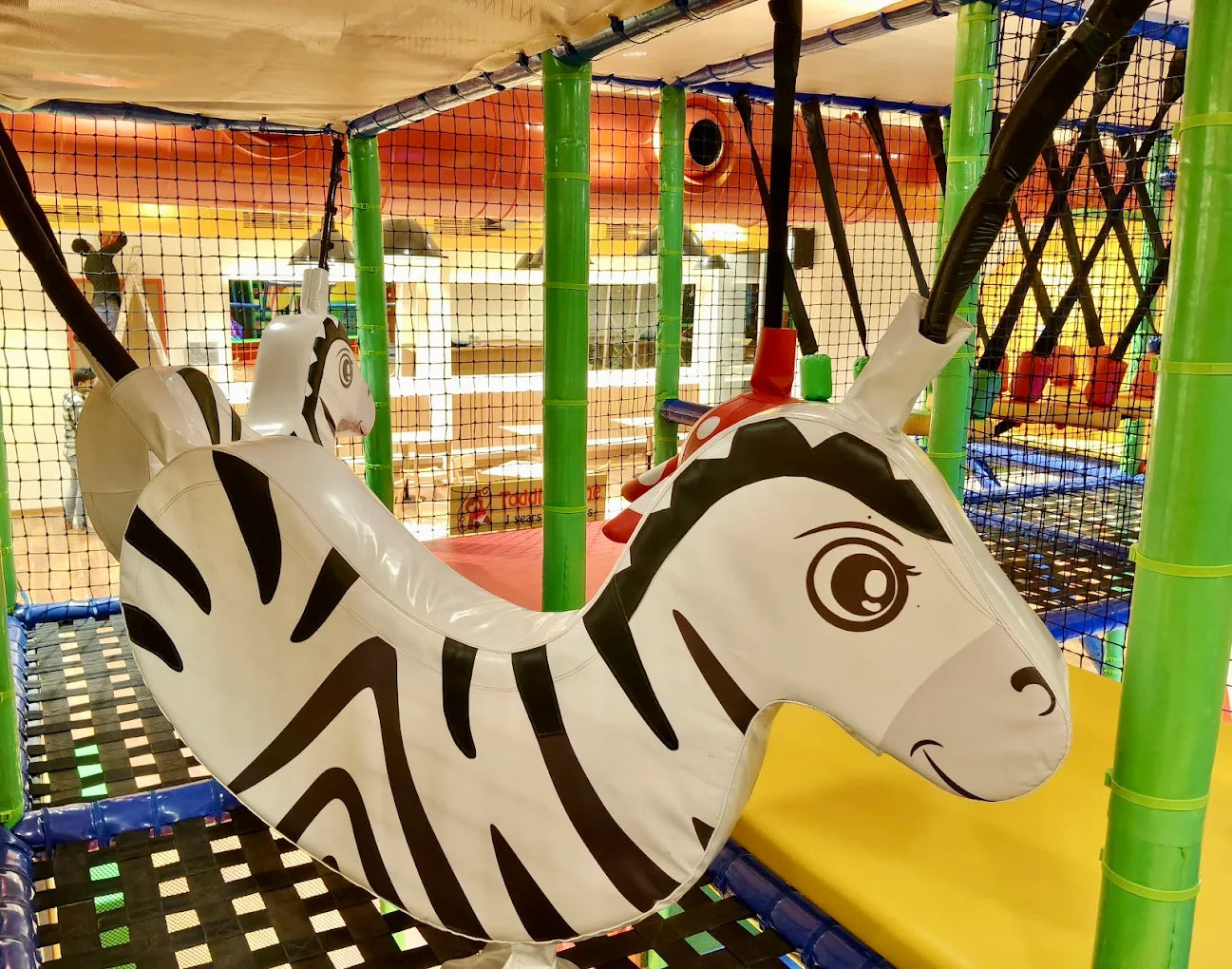 A large inflatable zebra swing hangs in a colorful indoor playground for children.