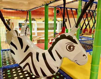 A large inflatable zebra swing hangs in a colorful indoor playground for children.