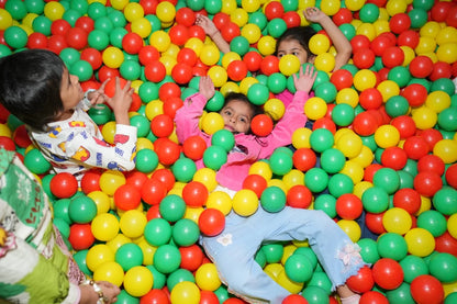 Children play in a ball pit filled with red, green, and yellow balls.