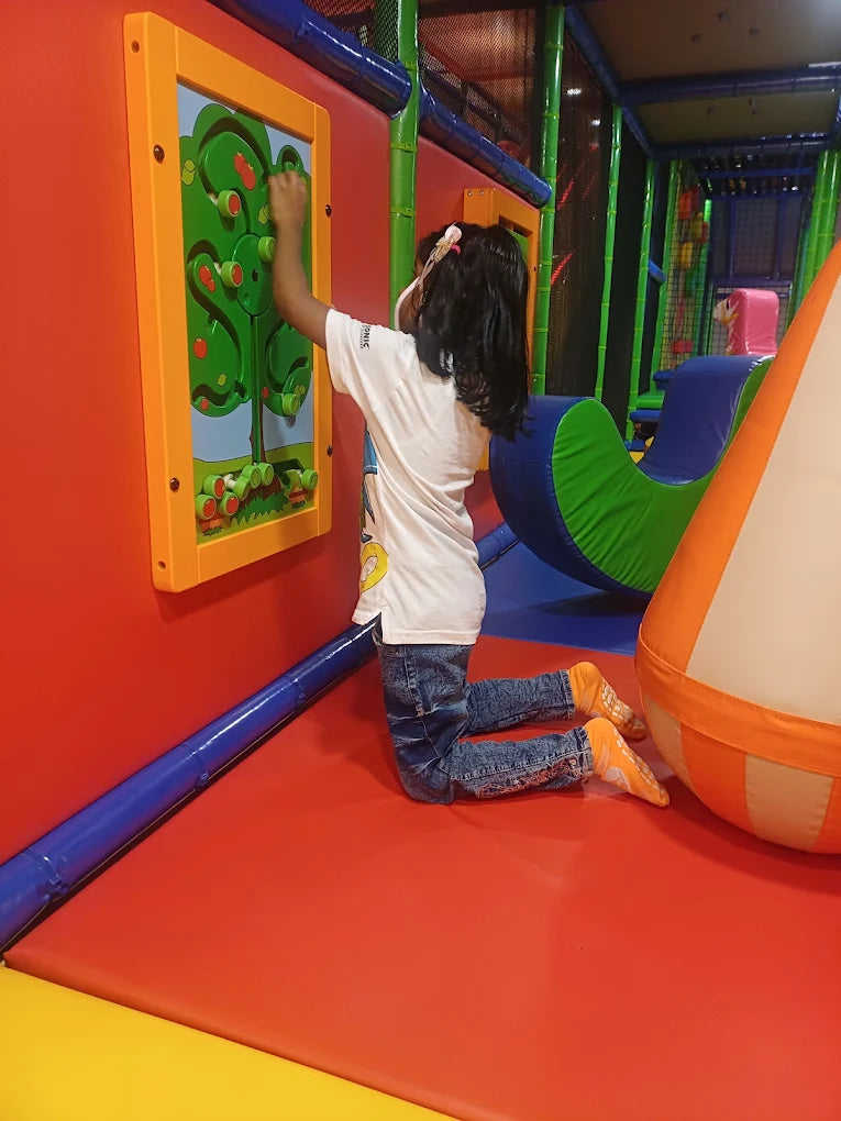 A young child plays with a colorful interactive wall game in a soft play area.
