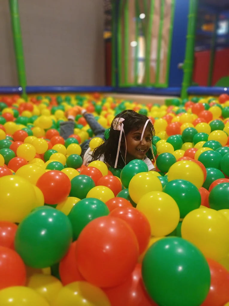 A young girl smiles while lying in a ball pit filled with colorful balls.