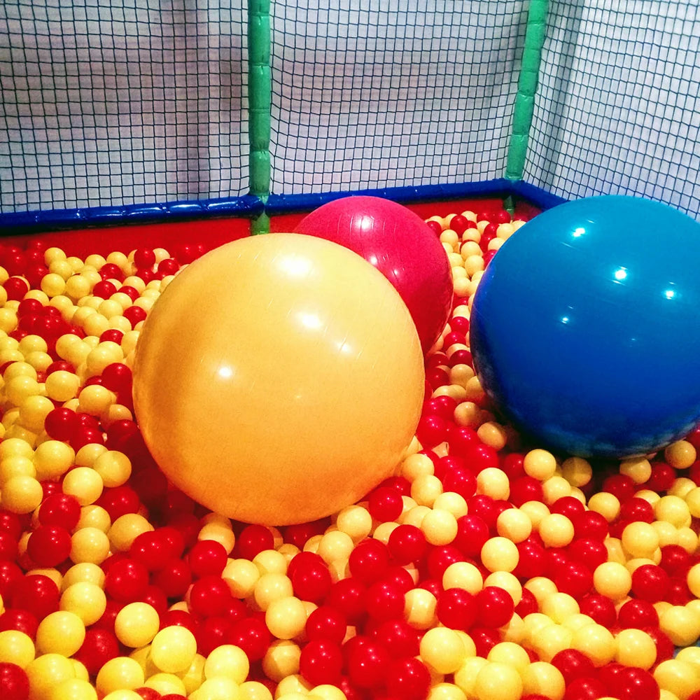 Three large inflatable balls (yellow, pink, blue) sit in a ball pit filled with small red and yellow balls.