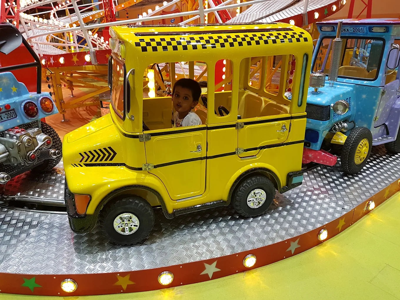 A young child sits in a yellow toy taxi on a carnival ride.
