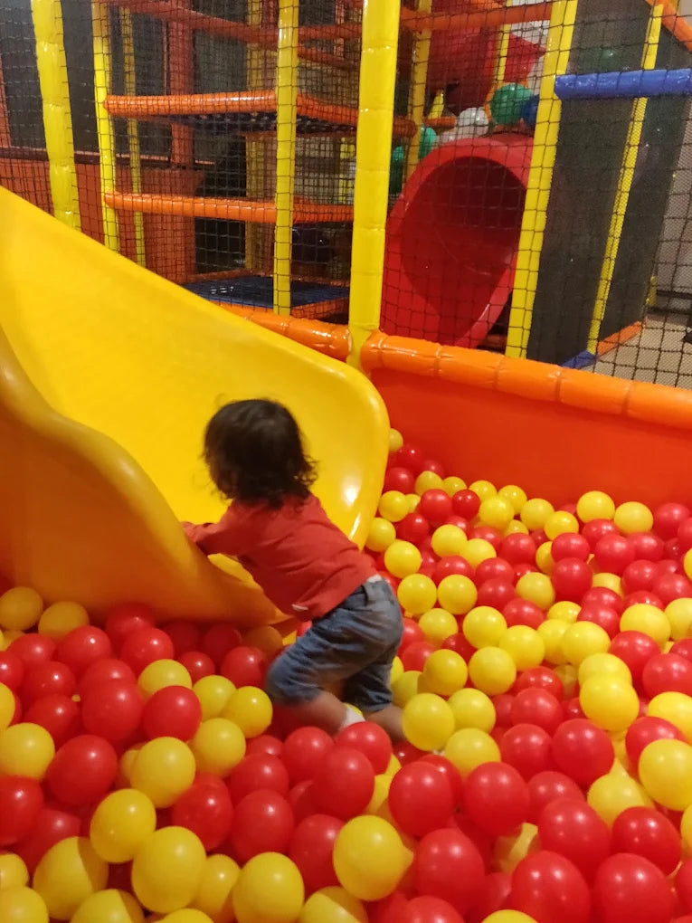A young child plays in a ball pit with a yellow slide.