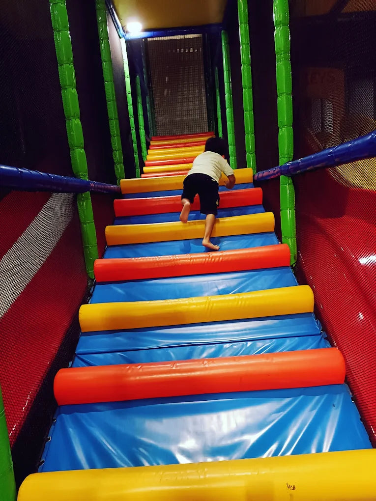 A child climbs a colorful, padded staircase in an indoor playground.