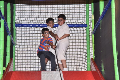 Three young boys play in a colorful indoor playground, pulling on a rope.