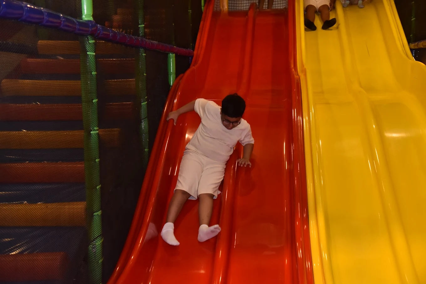 A young boy slides down a red playground slide next to a yellow slide.
