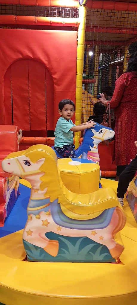 A young child rides a carousel horse in a colorful indoor play area.