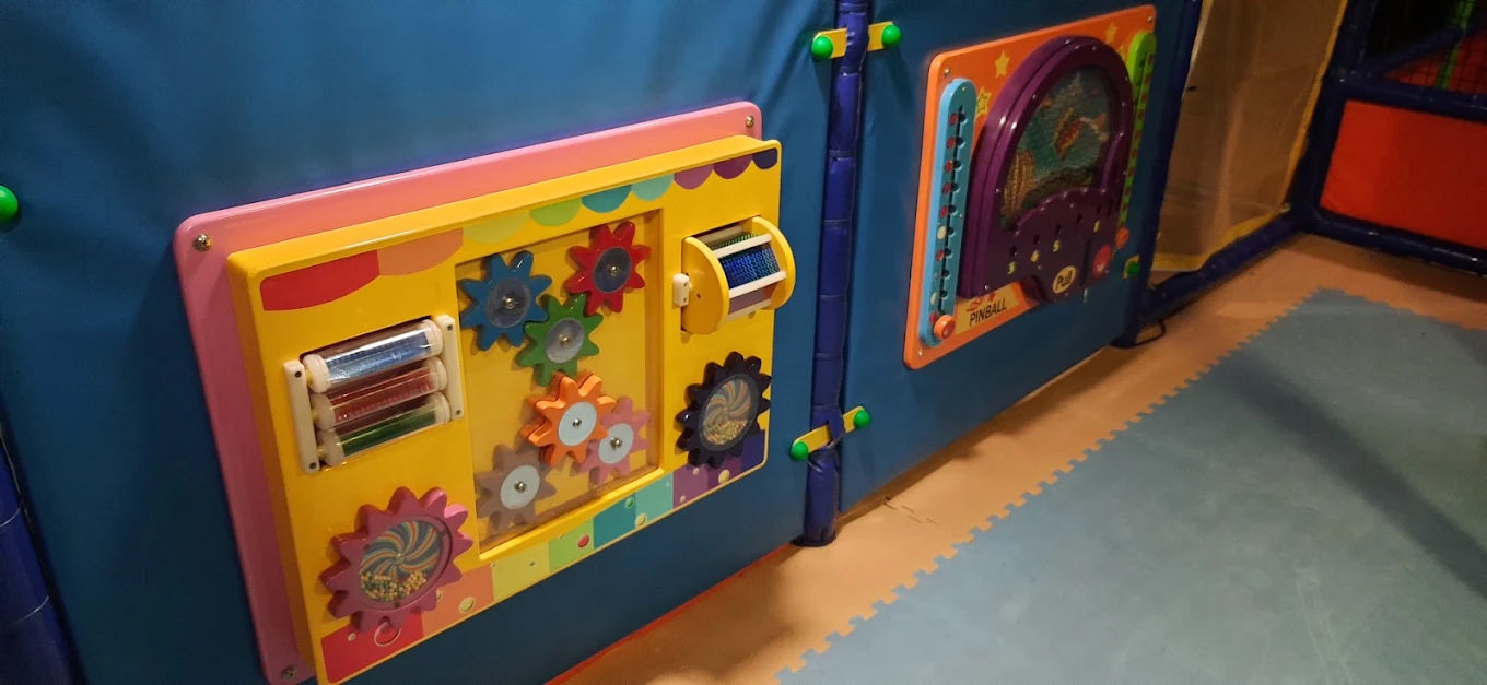 Interactive play wall with gears and a pinball game for children.