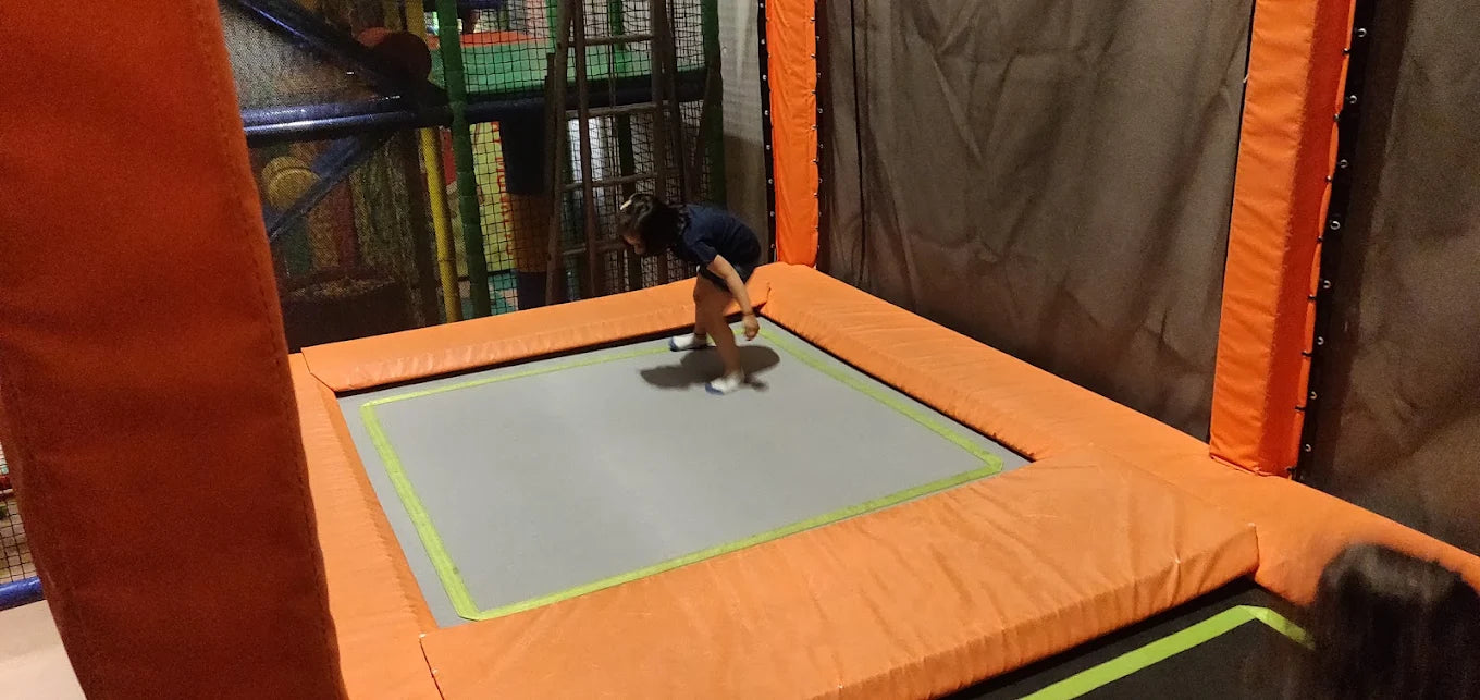 A child bounces on a trampoline in an indoor play area.