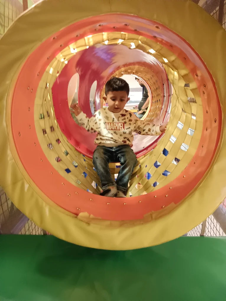 A young boy sits in a colorful play tunnel, wearing a Marvel sweatshirt.