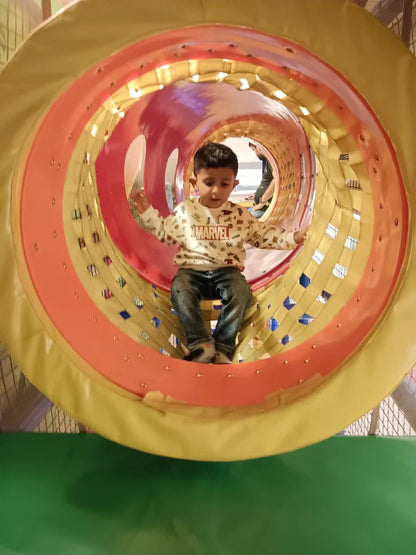 A young boy sits in a colorful play tunnel, wearing a Marvel sweatshirt.