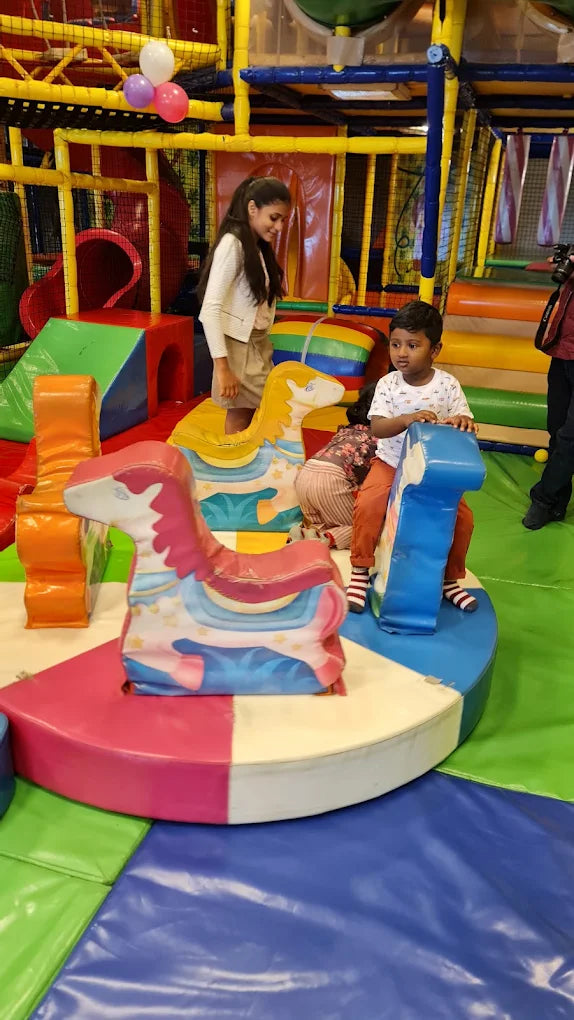 Children play on a colorful carousel in an indoor playground.
