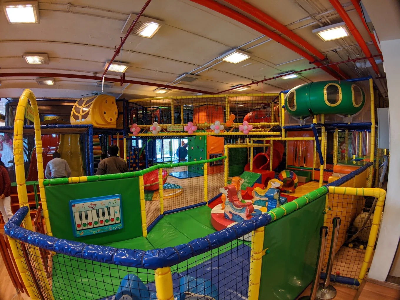 A colorful indoor playground with children's play structures and a few adults.
