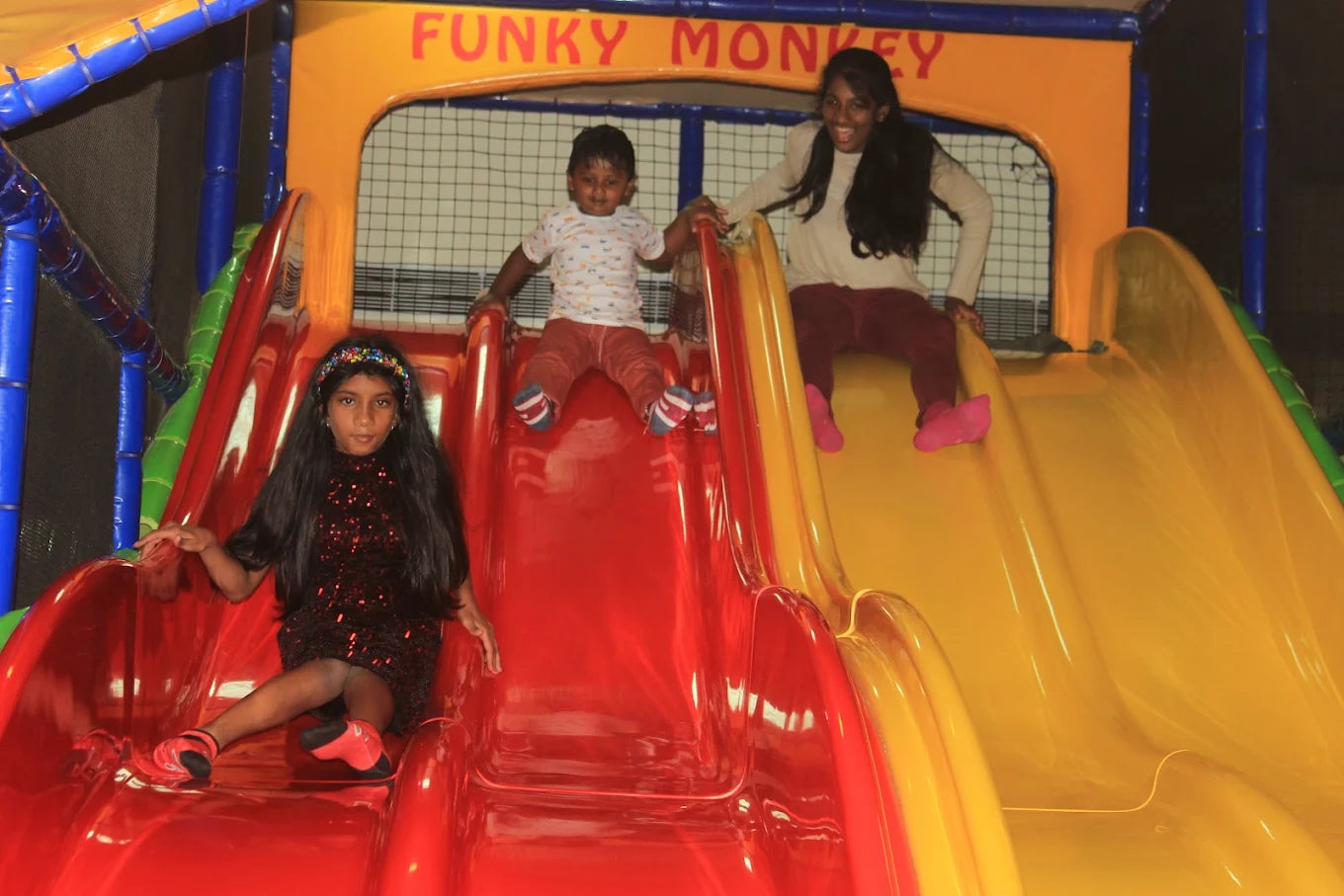 Three children slide down a colorful playground structure.