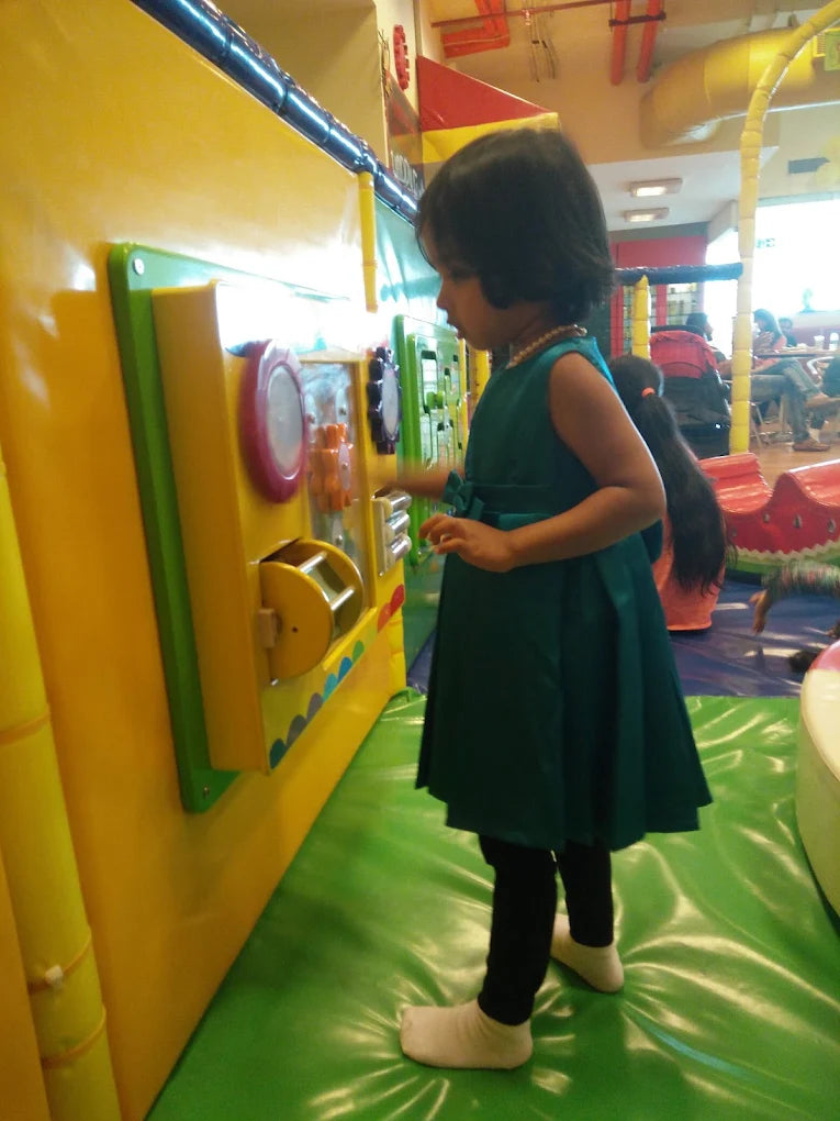 A young child plays with a colorful interactive wall in a brightly lit indoor play area.