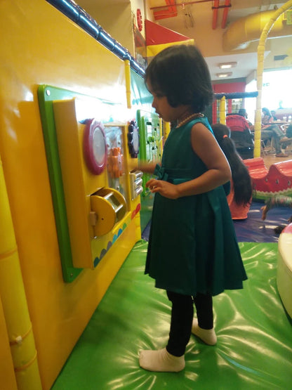 A young child plays with a colorful interactive wall in a brightly lit indoor play area.