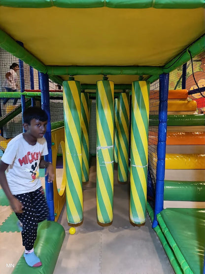 A young boy plays in a colorful indoor playground with soft pillars and climbing structures.
