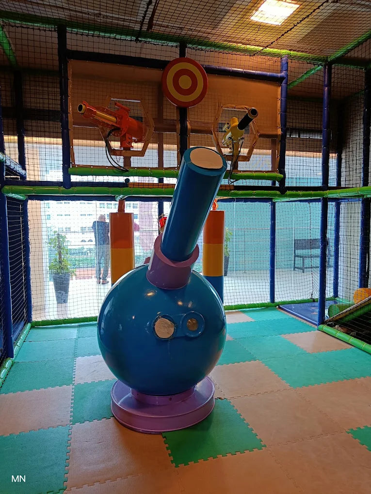 A colorful indoor playground with a large blue cannon and two toy guns.