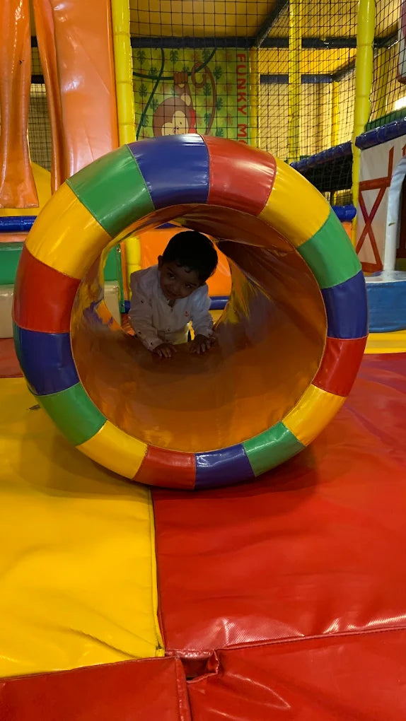 A young child crawls through a colorful tunnel in a soft play area.