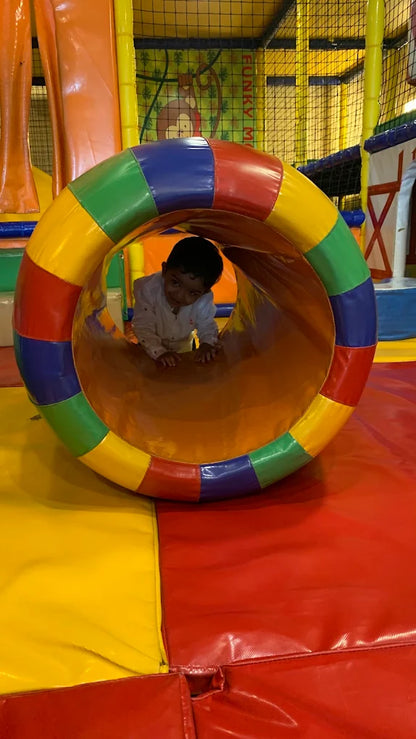 A young child crawls through a colorful tunnel in a soft play area.