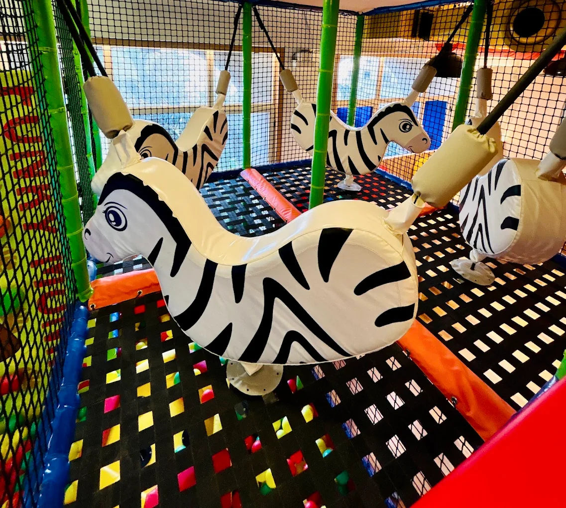 Soft zebra-shaped swings hang in a colorful indoor playground for children.