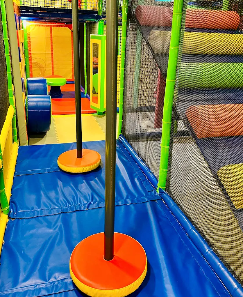 Indoor playground with colorful padded obstacles and poles for children.